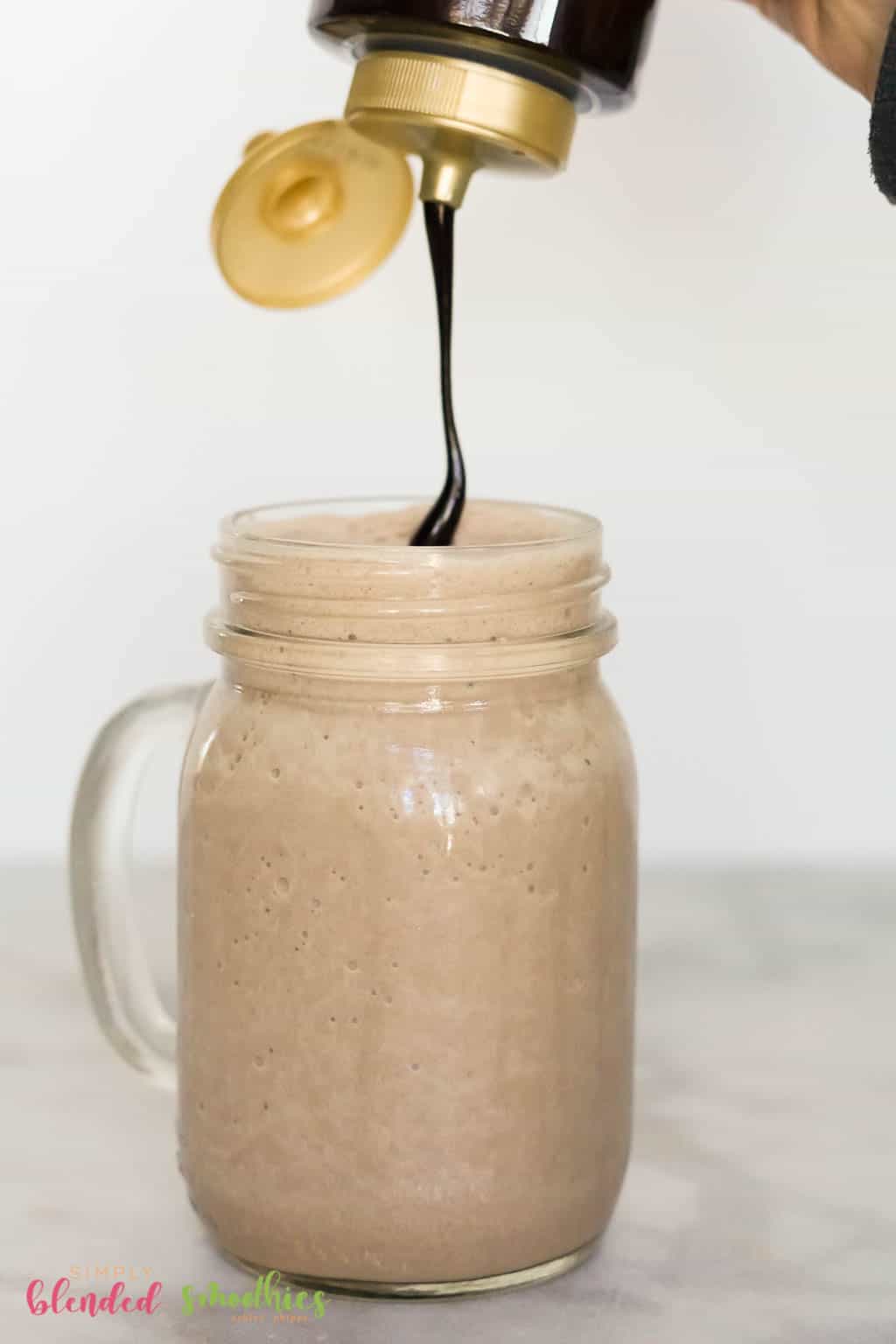 Drizzling Chocolate Syrup On Top Of A Chocolate Frappuccino In A Mason Jar Glass