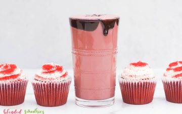 red velvet shake with chocolate syrup dripping down the side chocolate flakes and red velvet cupcakes on the side