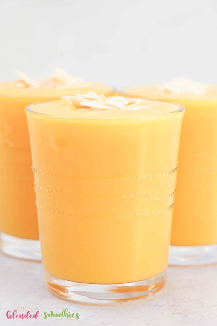 Close Up Vertical Photo Of Mango Peach Smoothie In A Clean Glass With Coconut Flakes On Top