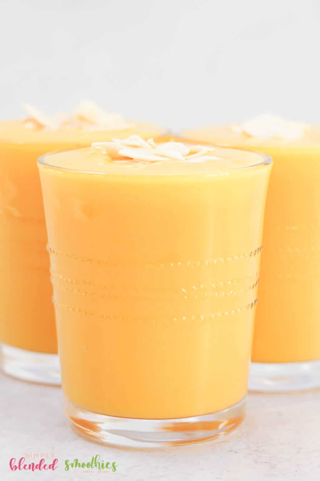 Close up verticale foto van mango perzik smoothie in een schoon glas met kokosschilfers bovenop