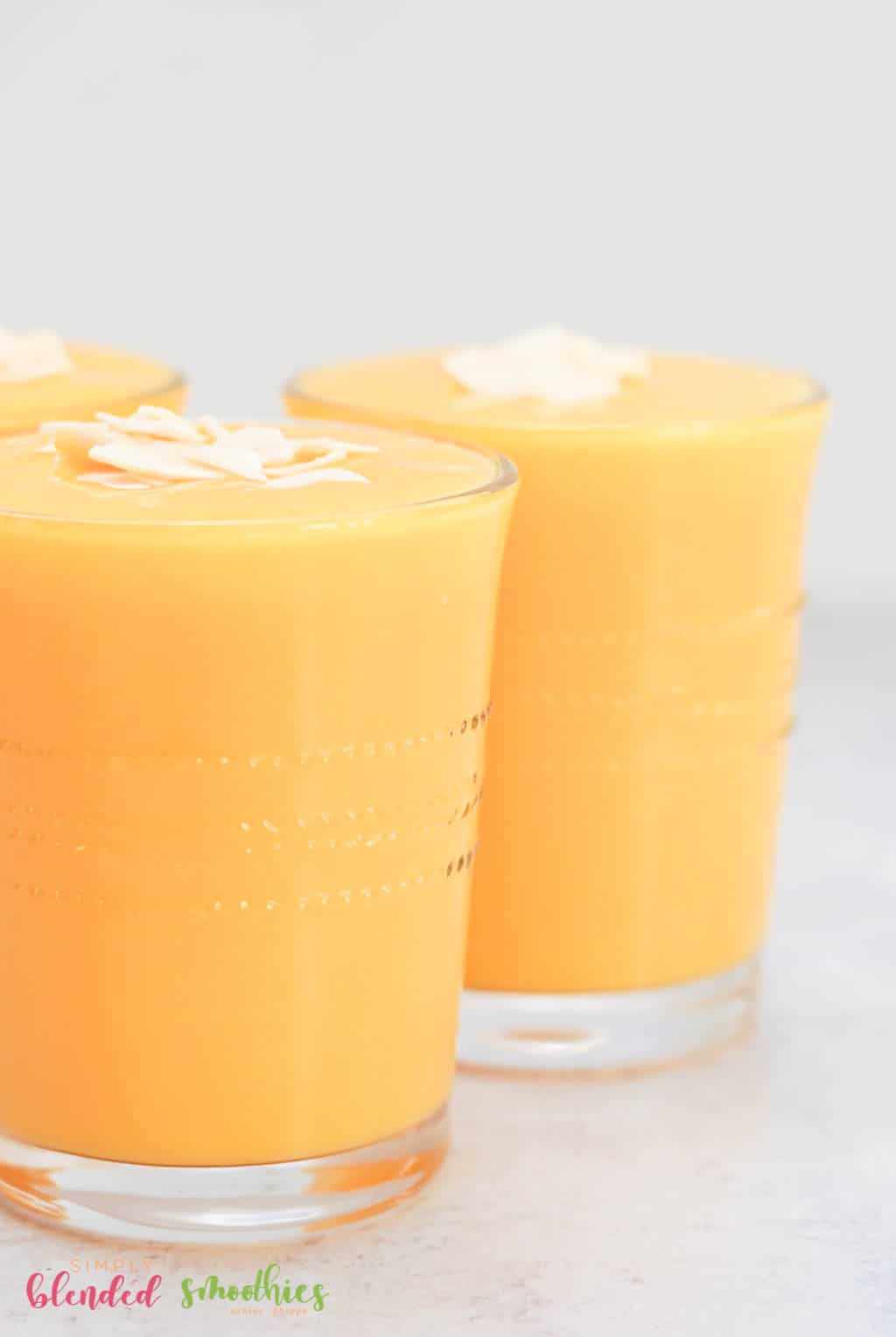 Side View Of Smoothie Made With Mangos And Peaches Topped With Coconut Flakes In A Clear Glass