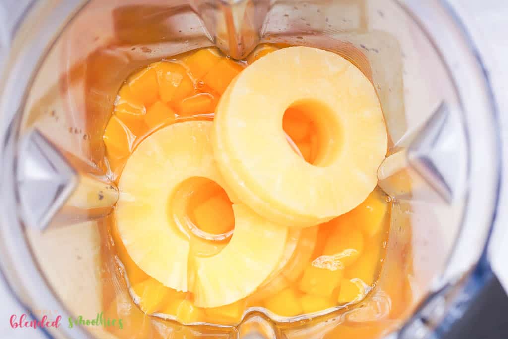 mango e ananás num liquidificador olhando de cima para baixo