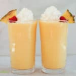 two pineapple peach milkshakes with whipped cream topping looking at them from the side in a horisontal photo