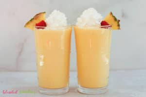 Two Pineapple Peach Milkshakes With Whipped Cream Topping Looking At Them From The Side In A Horisontal Photo