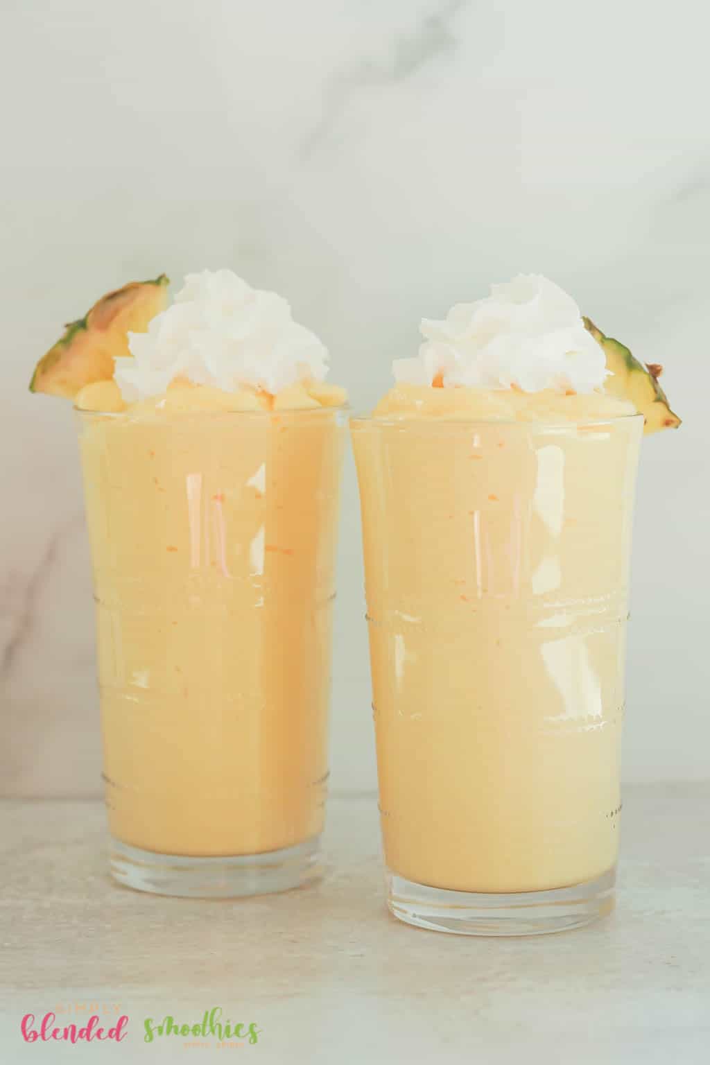 Two Milkshakes Made With Pineapple And Mango And Topped With Whipped Cream And Pineapple Slice