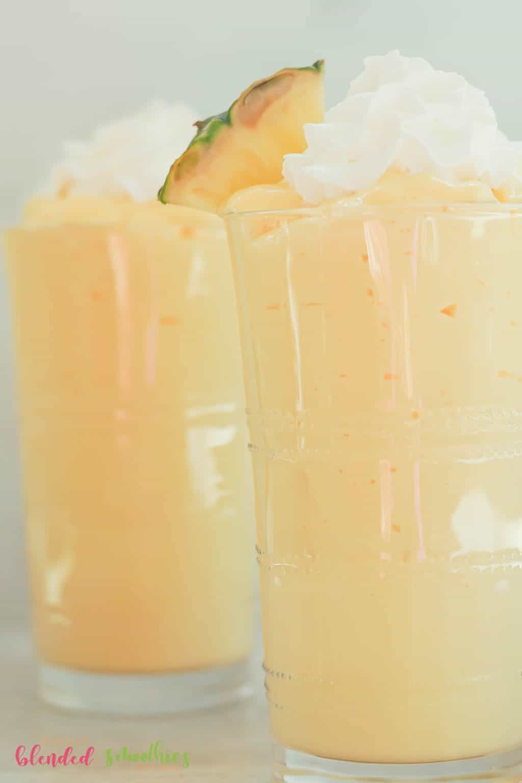 Close Up Vertical Photo Of Milkshake Made With Mangos And Pineapple Topped With Whipped Cream And A Fresh Pineapple Slice